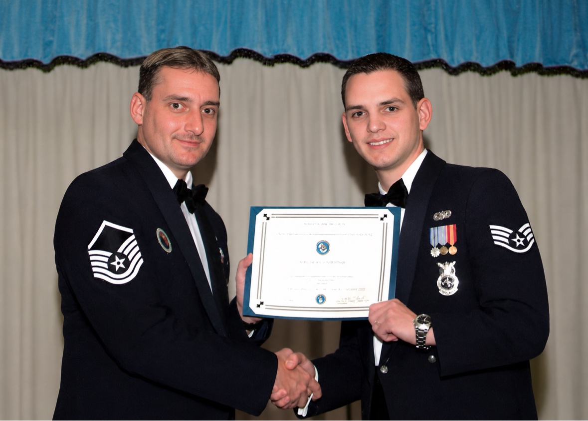 Jason McClaren in Air Force dress uniform receiving an award certificate and shaking hands