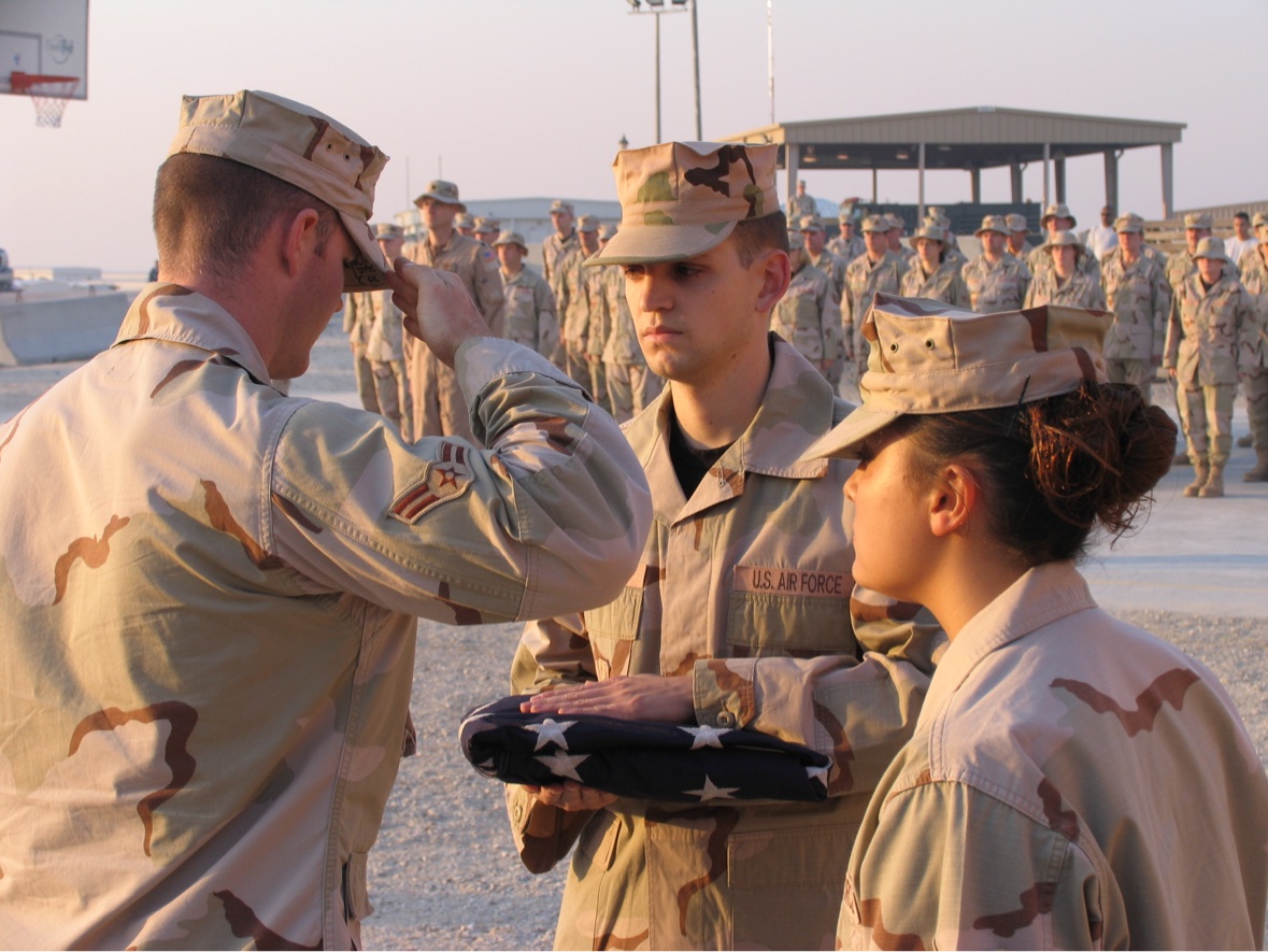 Jason McClaren in desert camouflage holding a folded American flag during a ceremony while deployed