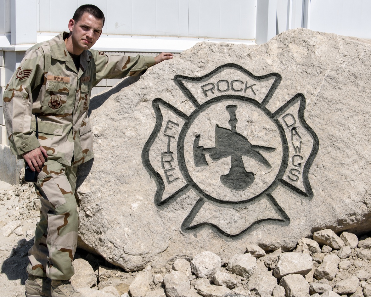 Jason McClaren in desert camouflage beside the Fire Dawgs rock